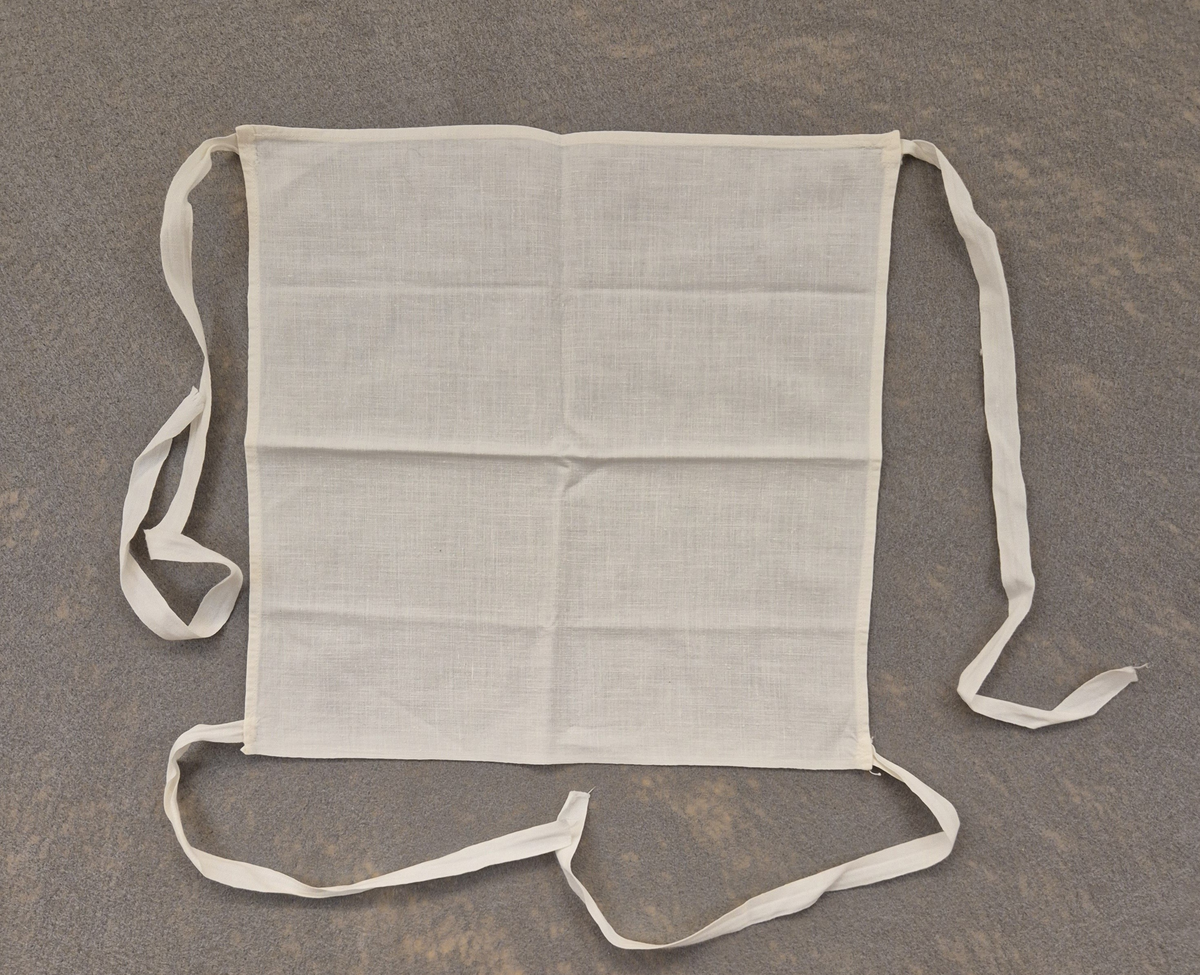 Munskydd i textil. Knyts med band från vardera hörn av munskyddet.

Till detta munskydd ingår en vit skyddsrock med långa ärmar samt ytterligare ett munskydd i textil. (VM29921)