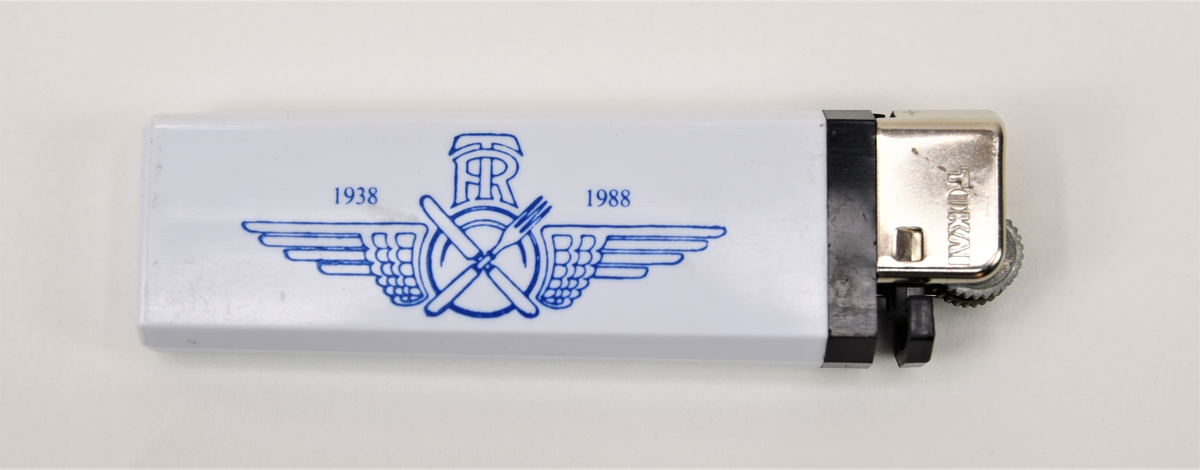 Tändare med kropp av vit och svart plast och metalldetaljer för gnist och låga. På metallen finns präglad text: "Tokai". 
TR:s logotyp är tryckt på tändarens kropp. Logotypen består av texten "TR 1938 - 1988" med en bevingad tallrik med korsad kniv och gaffel.