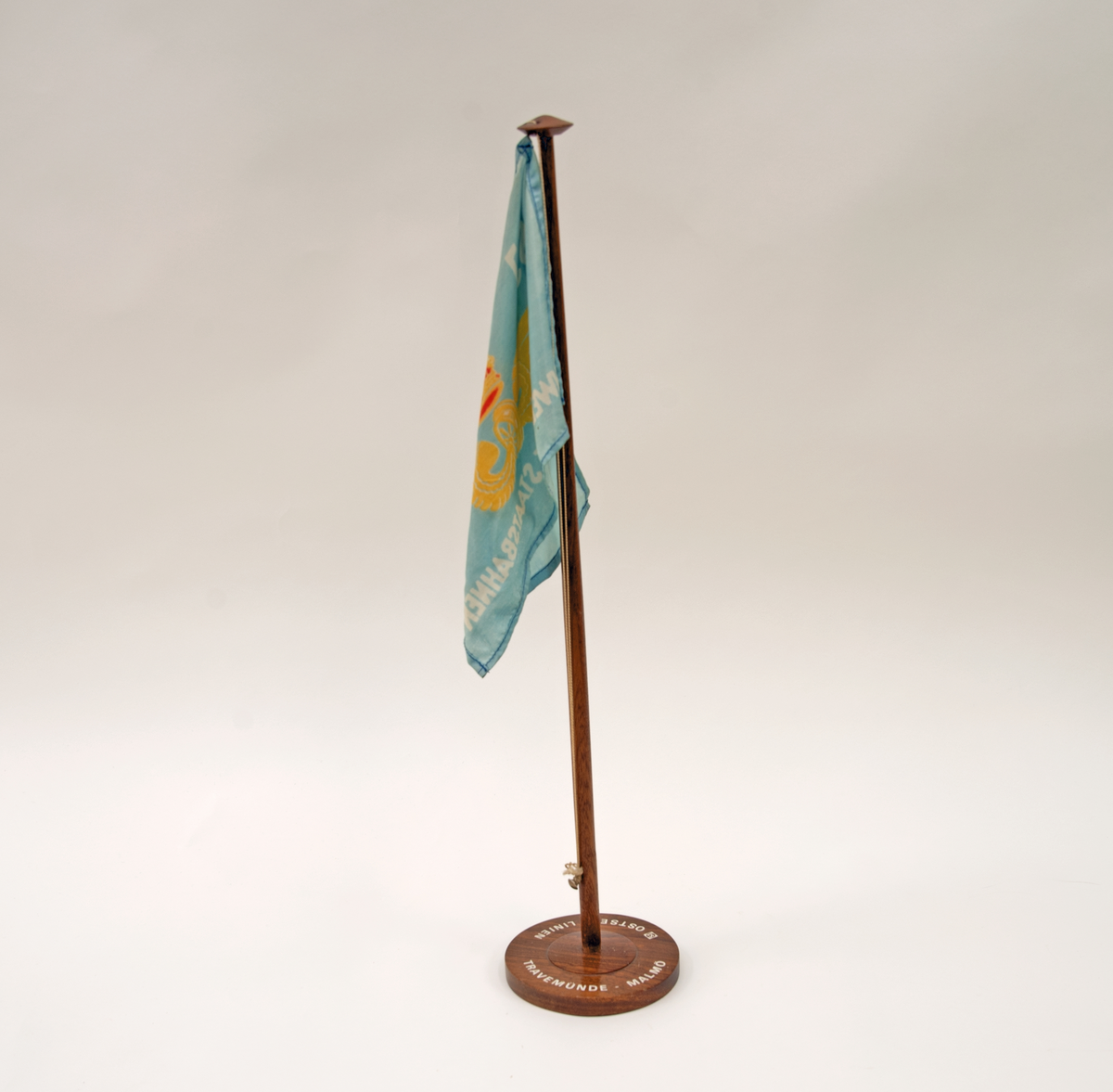 Bordstandar med blå flagga med SJ:s logotyp och texten: "SCHWEDISCHE STAATSBAHNEN". Stång och fot av trä, på foten tryckt text: "SJ OSTSEE - LINIEN" "TRAVEMÜNDE - MALMÖ".