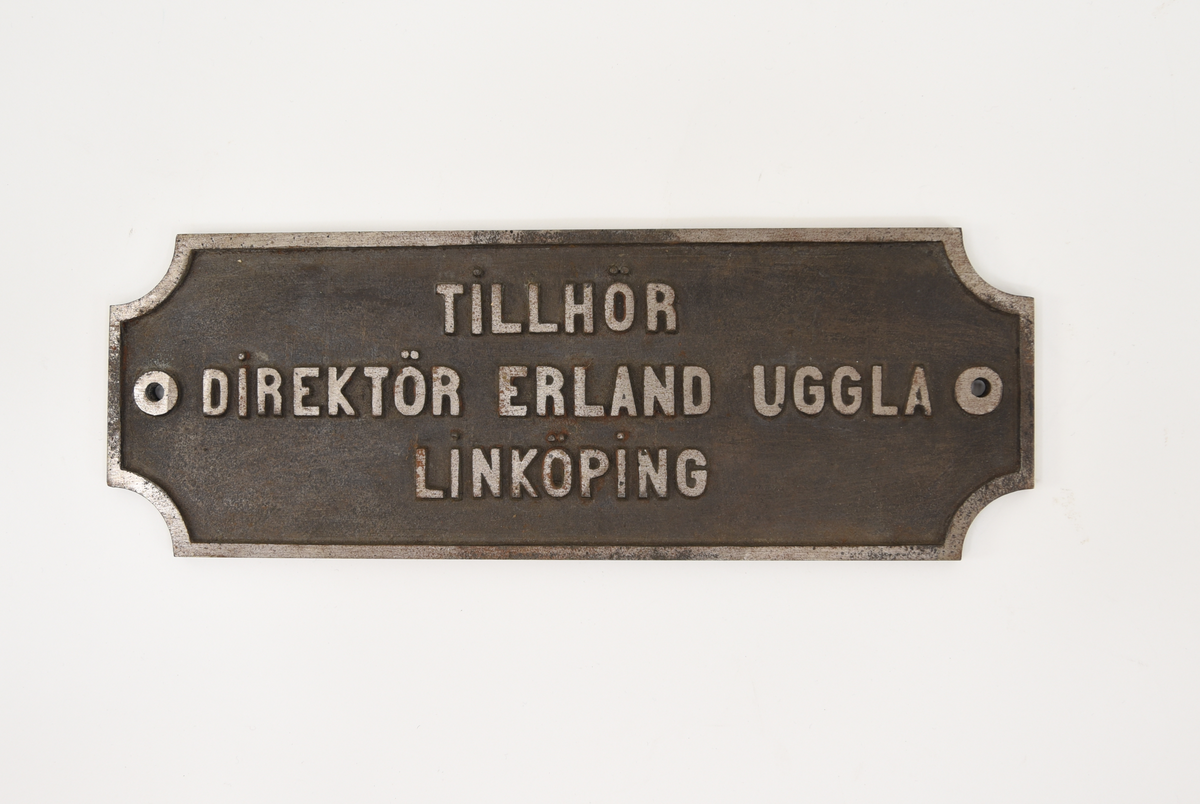 Namnskylt av metall med texten: "TILLHÖR DIREKTÖR ERLAND UGGLA LINKÖPING"