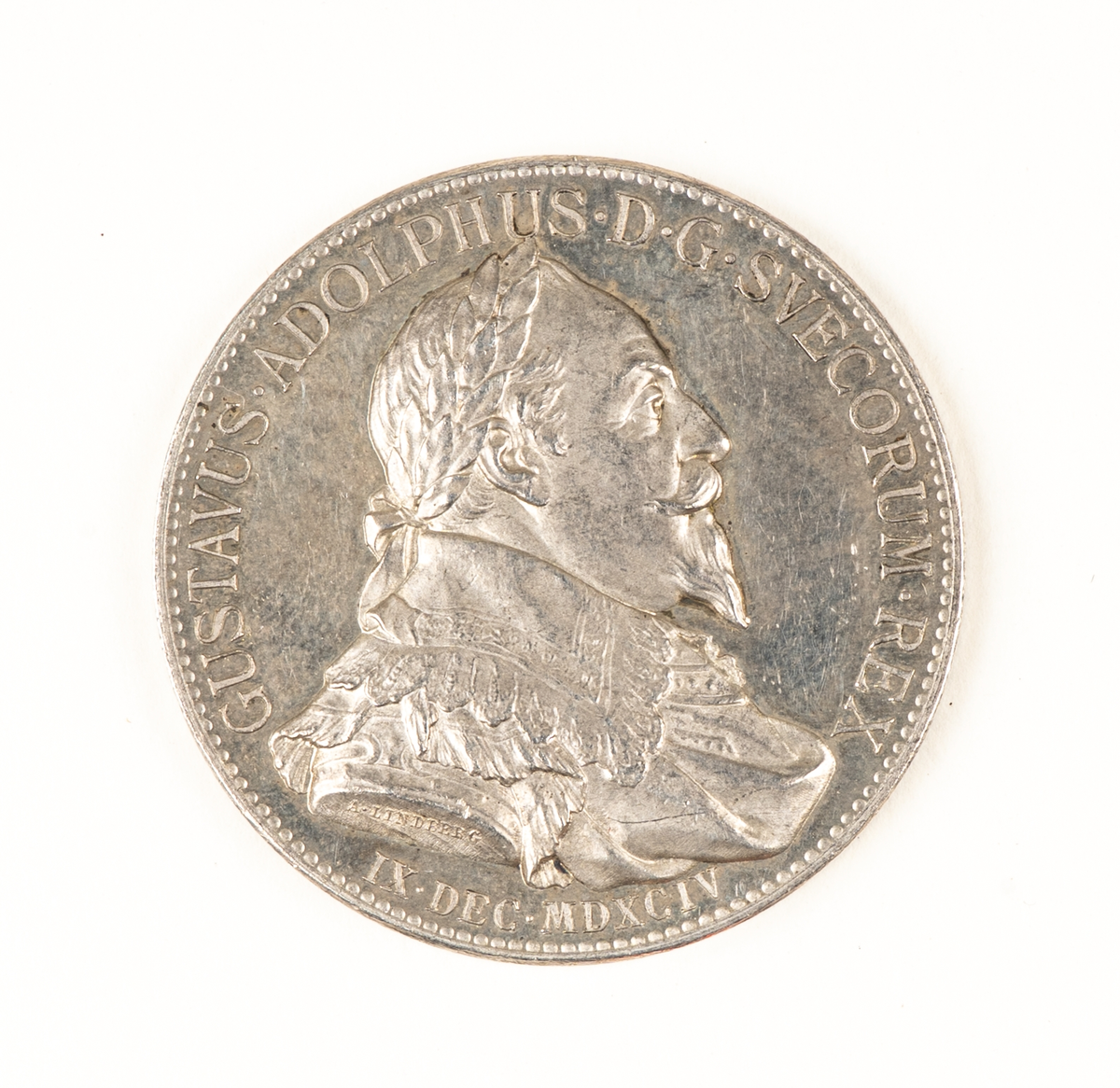 Medalj, minnespenninge i silver till 300-årsminnet av Gustaf II Adolfs (regent 30.10.1611–6.11.1632) födelse. 

Åtsidan: GUSTAVUS . ADOLPHUS. D.G. SVECORUM. REX. IX. DEC. MDXCIV. Bröstbild åt höger i harnesk med mantelveck och bred spetskrage, huvudet bart, lagerbekransat. 
Frånsidan: En upptill öppen, nedtill med bandrosett hopfästad lagerkrans, inuti vilken läses: CUM DEO ET VICTRICIBUS ARMIS på 4 rader. Nedanför kransen IX.DEC.MDCCCXCIV, allt omgivet av en pärlrand.