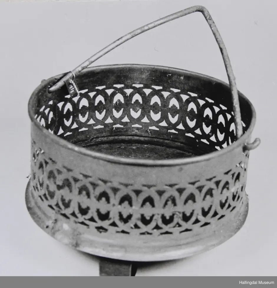 Botn er ei rund jarnplate. 3 føter, festa gjennom botnen. Sidene er av messing, ornamnetikk, masse hol av ulik fasong rundt etter kanten. Hank festa i 2 hol i messingsidene, hank av jarn.