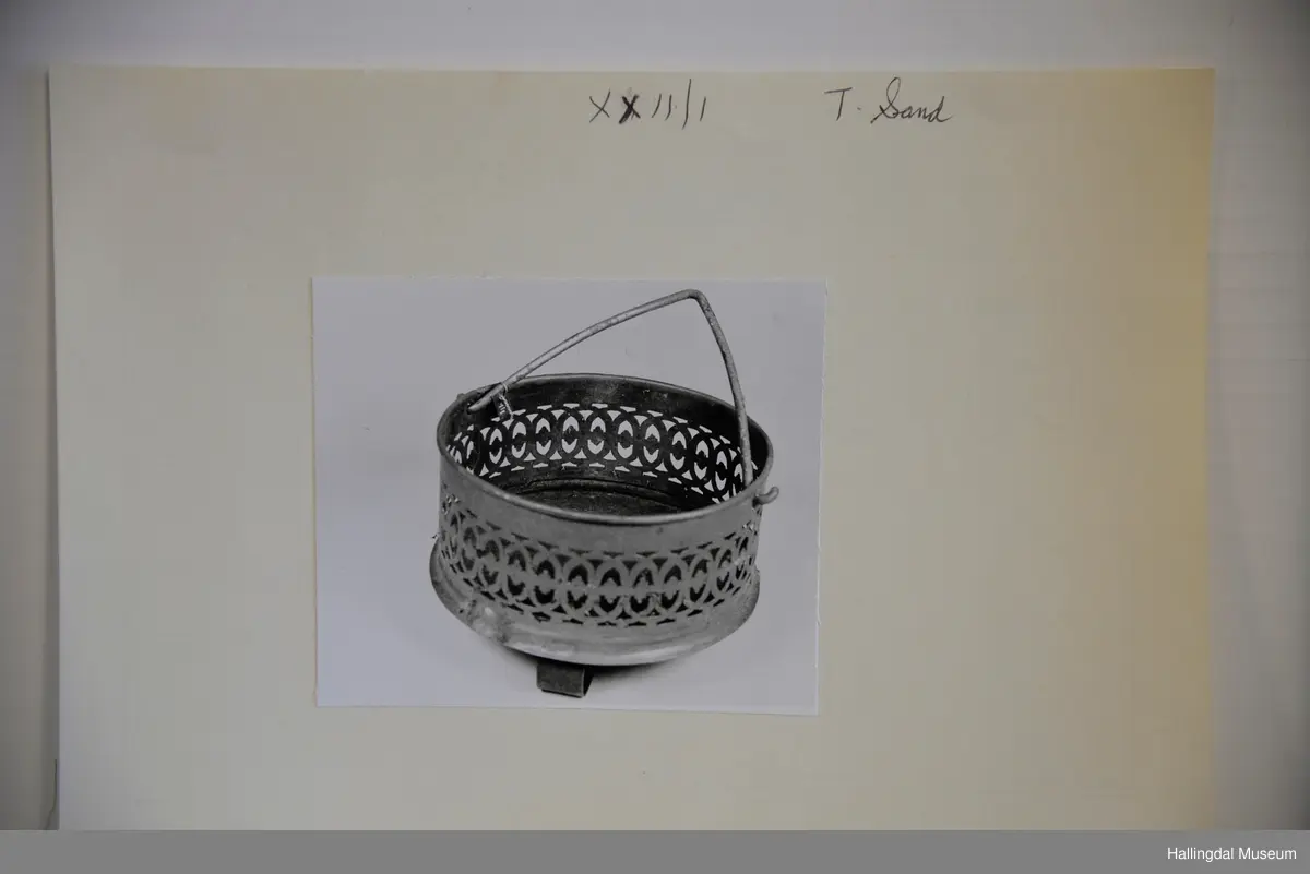 Botn er ei rund jarnplate. 3 føter, festa gjennom botnen. Sidene er av messing, ornamnetikk, masse hol av ulik fasong rundt etter kanten. Hank festa i 2 hol i messingsidene, hank av jarn.