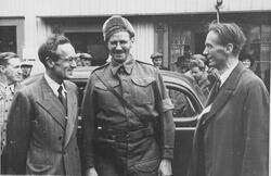 Tre menn foran en bil. Mannen i midten er mulig Otto Pahle. I bakgrunnen sees flere andre personer.