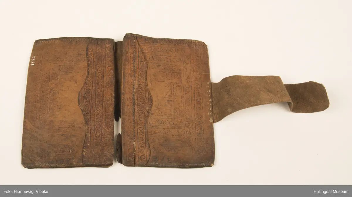 Lær, sydd. Langt rektangulært stykke brettet inn i begge ender. H oppslått: 21,8 cm, H gjenlukket: 17,1 cm, b lærreim: 4 cm.