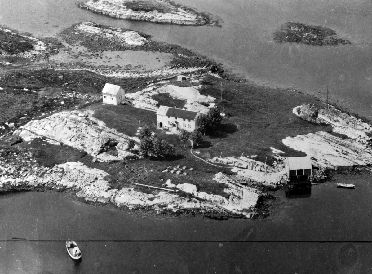 Flyfoto av et våningshus ute på en holme/øy, ukjent hvor. Reprofotografiet er registrert på navnet Olav Breivik i 1964. Fra fotoarkivet etter portrettfotograf Claus Monge. Museet overtok arkivet sommeren 2011.