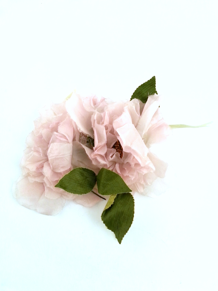 Fotsid kjole med antydning av slep. Sydd av taft, overtrukket med blomstervevd tyllblonde. Livstykket er glatt, mens det vide, utskrådde skjørtet består av umønstret tyll, påsydd overlappende kapper av blomstervevd tyllblonde; 12 kapper bak og ni foran, de øverste smalere og de nedre gradvis bredere. Under dette, mellom taft og tyllkapper; et lag gammelrosa tyll. Overdelen er avstivet av tilsammen sju isydde spiler. Livstykket har tungeformet avslutning i overkant, samt på det beltelignende partiet over mellomgulvet, som går over i et separat belte på ryggpartiet. Stoffet over bysten er symmetrisk foldelagt under hvert bryst og asymmetrisk overlappet midt foran. Sammenføyningens, beltets og livstykkets tungeformede ytterkant er overkastet med klare glassperler tredd på en tråd. Kjolen er lavt skåret i ryggen og lukket med metallglidelås og en liten hekte. Bukett av tre blekrosa silkeblomster med grønne blader hører til. Den er nå løs, og har fått separat NK-nummer (NK2014-116), men satt opprinnelig i overkant av venstre bryst.