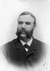 Foto av en okänd skäggprydd herre i randig kavaj. 
Bröstbild, halvprofil. Ateljéfoto.
Reprofoto efter äldre foto, ca 1890.