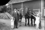 Foto av en lantbrukare med två barn, tre hästar och en ung dräng (?).
I bakgrunden syns en lada.