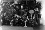 Foto av en man i uniform som sitter i ett vardagsrum, omgiven av mängder av blommor och presenter.