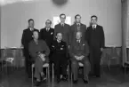 Foto av åtta män i kostym och uniform som samlats i en sal.
Föreningsstyrelse (?).