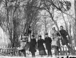 Sju ungdomar utomhus i vinterlandskap. På negativkuvertet står: "Carlsson, Lindahl, Thuresson vid träden utanför Linderbergs. 13 april 1895".