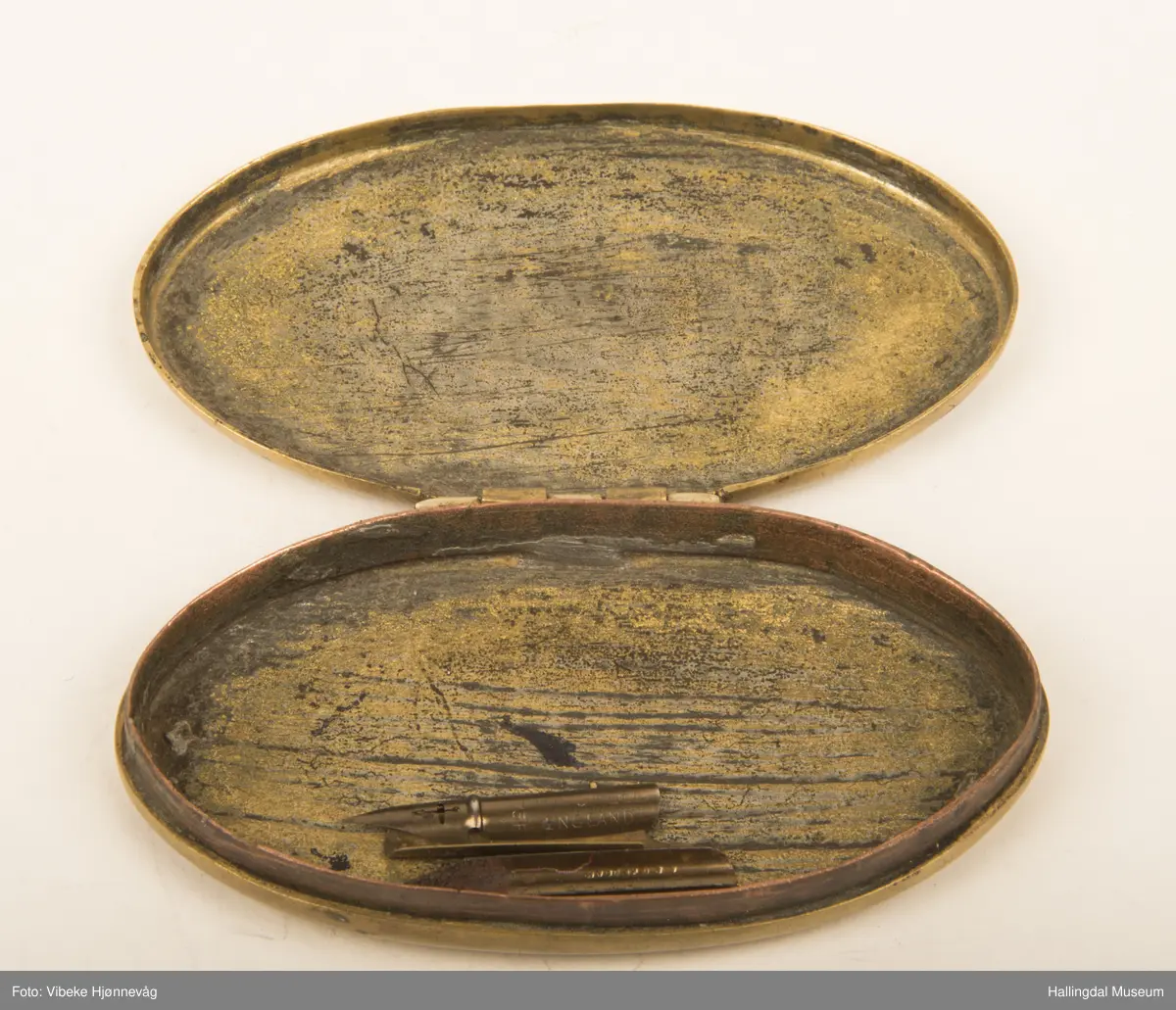 Messing, støpt. Oval, flat bunn, svakt hvelvet. Hengslet lokk. Ingen dekor. L: 9,3 cm, B: 5,3 cm.