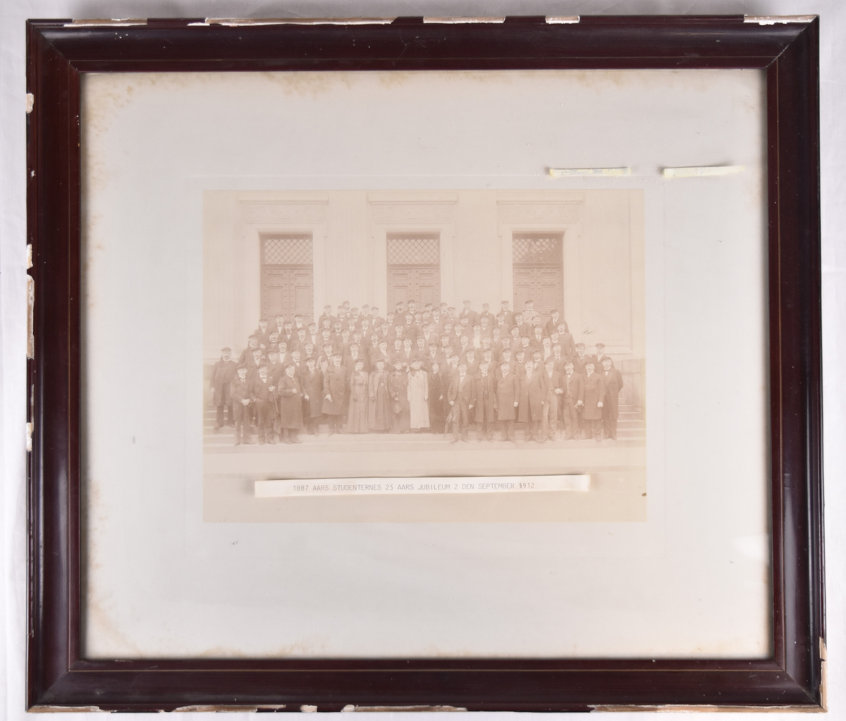 Innrammet fotografi av 25-årsjubileeet til 101 studenter fra 1887. Liste med navn står bakpå bildet.