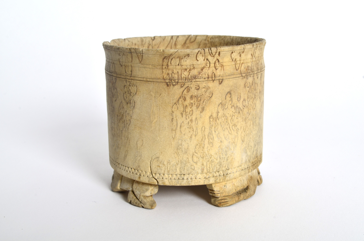 Sukkerkopp (?) i valbjørk. Dreid. Sylindrisk form, flat bunn. Rundt øverste kant, markerte dreiespor. Nederst, en innskåret, smal siksakbord. Står på tre bein som er skåret ut som liggende løver.