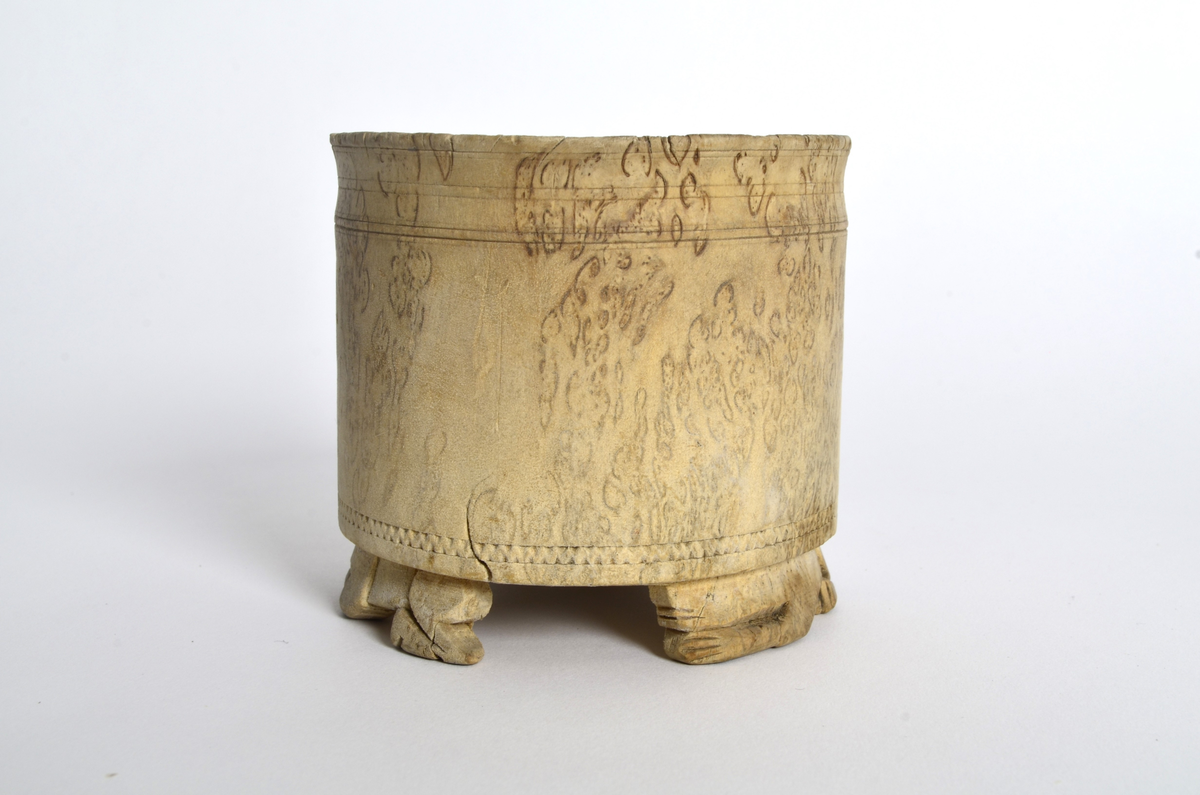 Sukkerkopp (?) i valbjørk. Dreid. Sylindrisk form, flat bunn. Rundt øverste kant, markerte dreiespor. Nederst, en innskåret, smal siksakbord. Står på tre bein som er skåret ut som liggende løver.