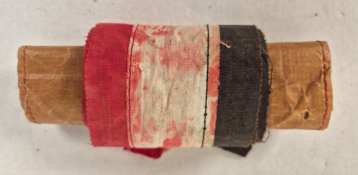 Pose med beskjed på tysk . Skrift og ornamentikk i Jugendstil (Art Nouveau)
Tekst: "Der Finder dieser Luftschiffpost wird höfl. gebeten den Innhalt dieser Tasche bei dem nächsten Postamte möglichst sofort abzuliefern".
Bånd er laget av tøy remser sydd sammen i fargene rød, hvit og svart.