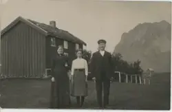 Et ektepar og en ung jente står utenfor et våningshus med to