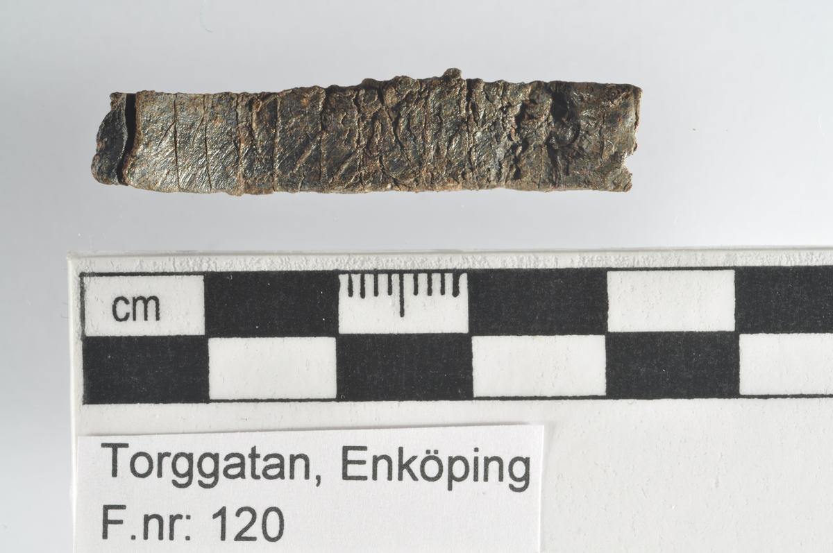 Föremål av metall. Bleck av bly. Avlångt, smalt och platt bleck. Runinskrift.