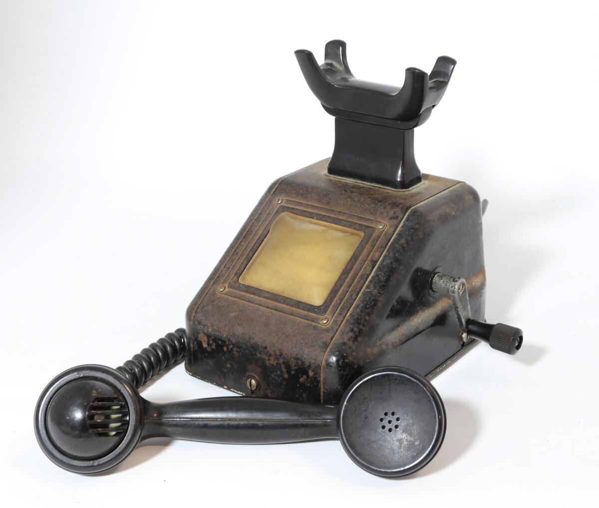 Telefonapparat for manuell sentral, brukt på setesdalsbanen. Apparatet har rektangulær bunn, rette sider, og skrå forkant med flat topp.  Det er en sveiv på siden, og ramme i front med plastdeksel.