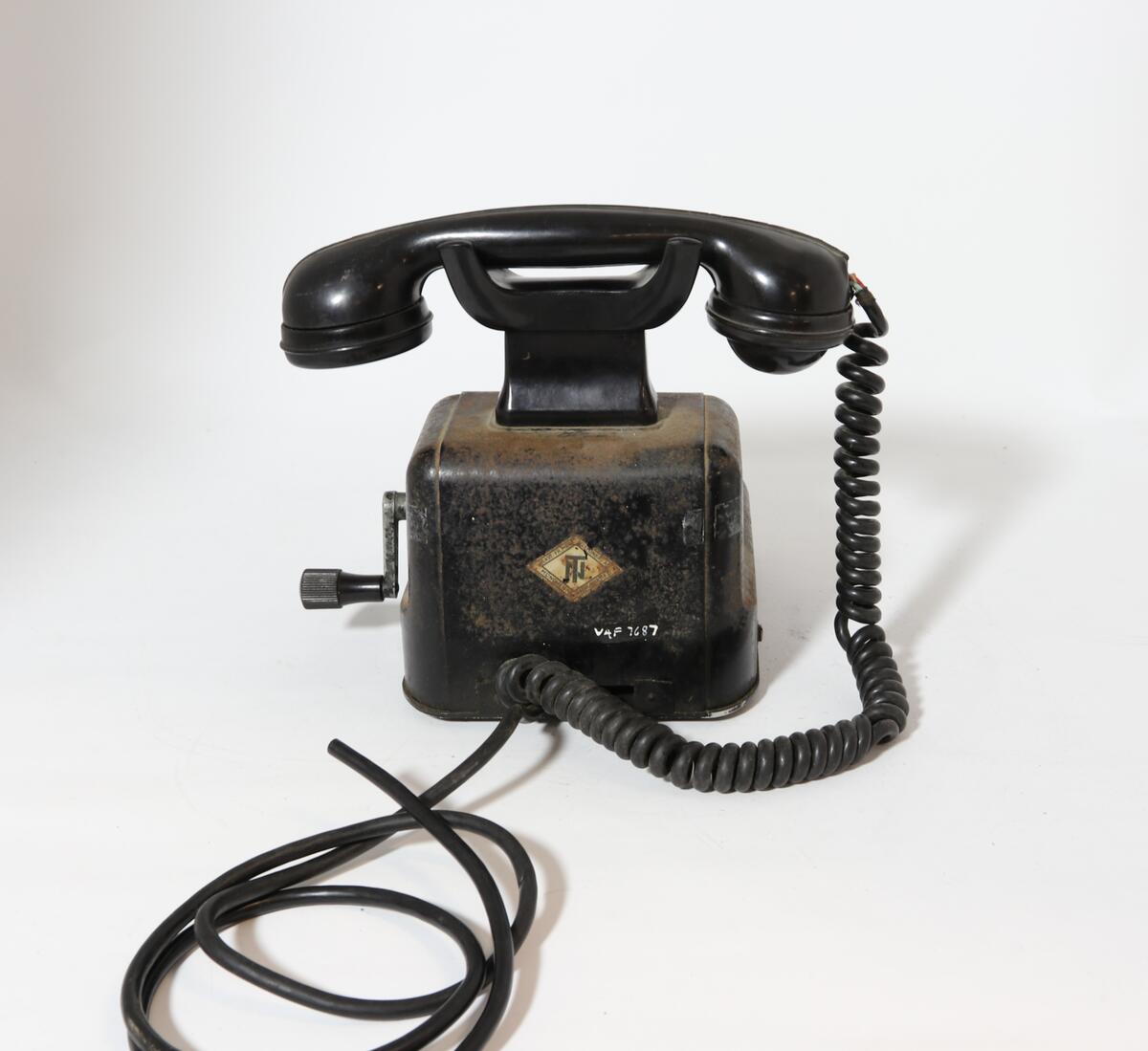 Telefonapparat for manuell sentral, brukt på setesdalsbanen. Apparatet har rektangulær bunn, rette sider, og skrå forkant med flat topp.  Det er en sveiv på siden, og ramme i front med plastdeksel.