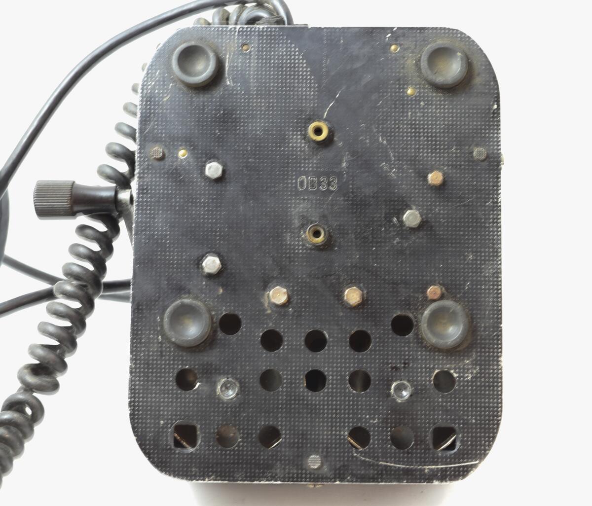 Telefonapparat for manuell sentral, brukt på setesdalsbanen. Apparatet har rektangulær bunn, rette sider, og skrå forkant med flat topp.  Det er en sveiv på siden, og ramme i front med plastdeksel.