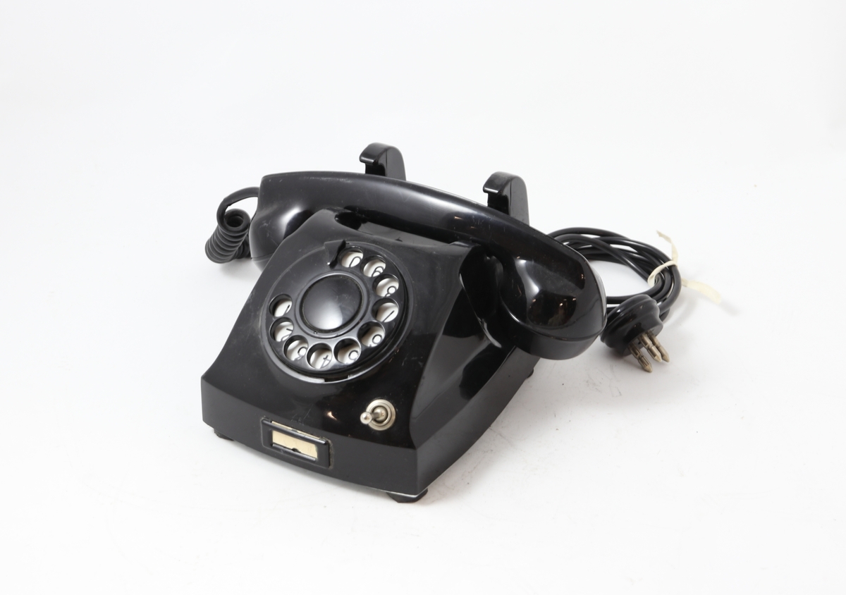 Svart bordtelefon med tallskive og bryter for å slå av inngående ringesignal
