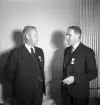 Sammanträde på Stadshotellet, 1943. 
Två herrar i kostym och med medaljer på kavajslaget pratar med varandra.