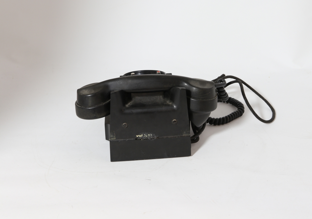 Vanlig bord-telefon med trykknapp under på siden av tallskiven. Telefonen har ekstra intern linje. Er et såkalt sekretærapparat. Telefonen er utstyrt med tekstilsnor til mikrofon og støpsel. To trykknapper ved gaffelen for intern linje.
