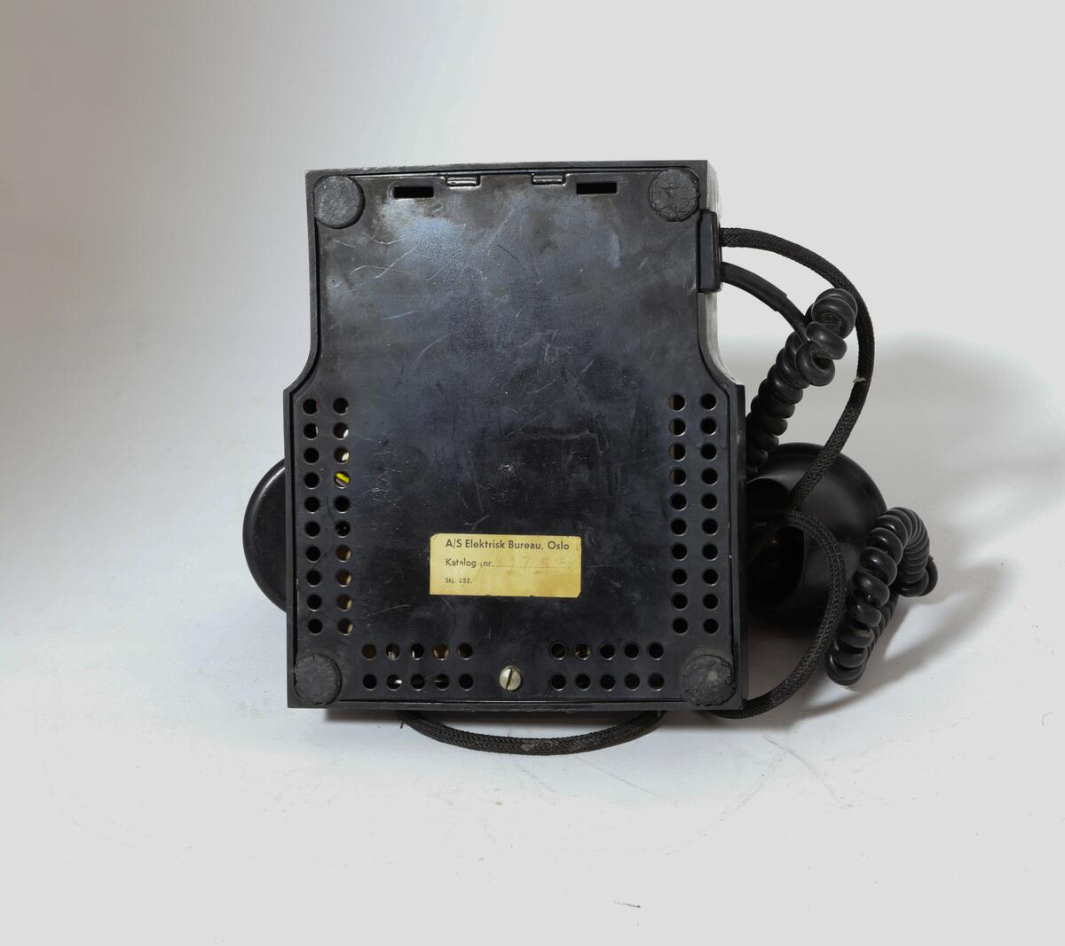 Vanlig bord-telefon med trykknapp under på siden av tallskiven. Telefonen har ekstra intern linje. Er et såkalt sekretærapparat. Telefonen er utstyrt med tekstilsnor til mikrofon og støpsel. To trykknapper ved gaffelen for intern linje.
