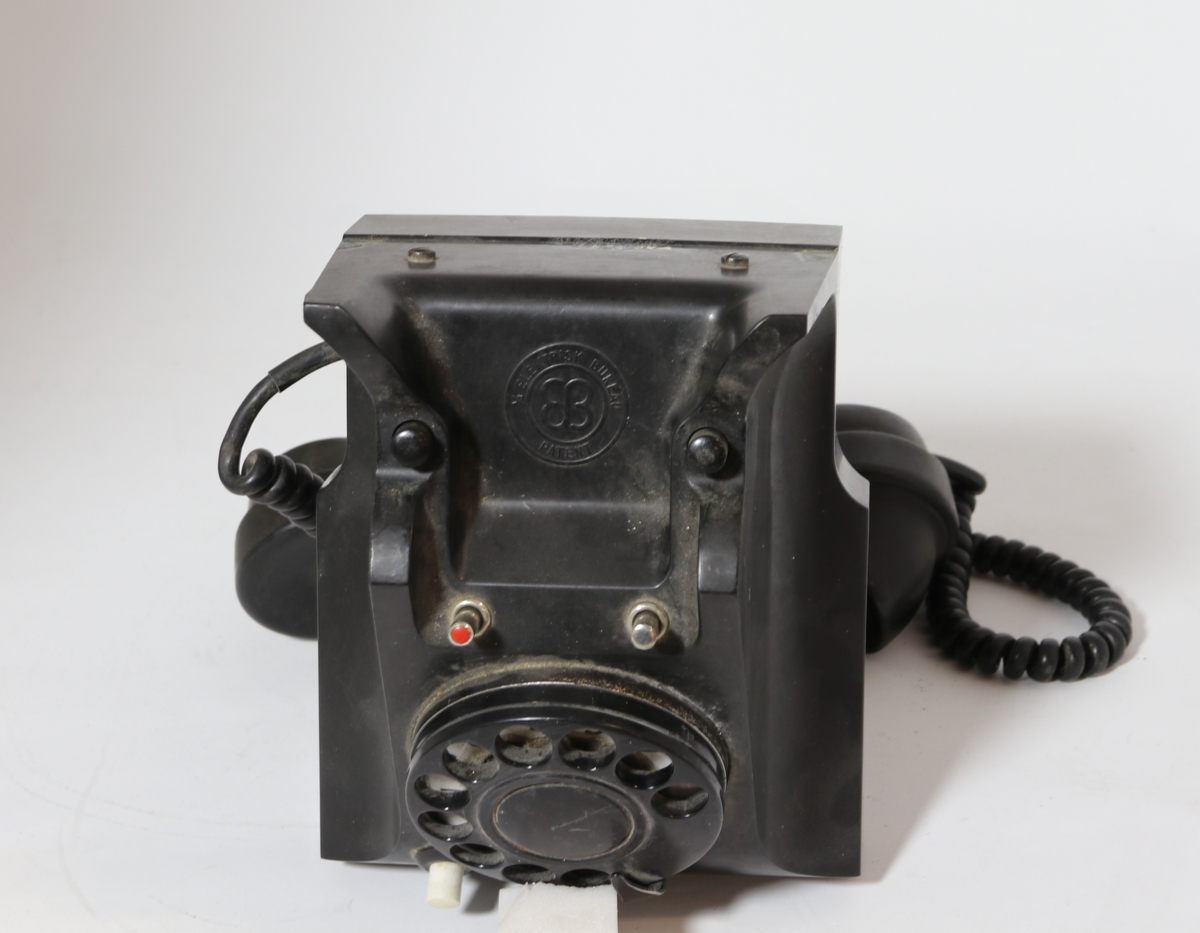 Vanlig bord-telefon med trykknapp under på siden av tallskiven. Telefonen har ekstra intern linje. Er et såkalt sekretærapparat. Telefonen er utstyrt med tekstilsnor til mikrofon og støpsel. To trykknapper ved gaffelen for intern linje.
