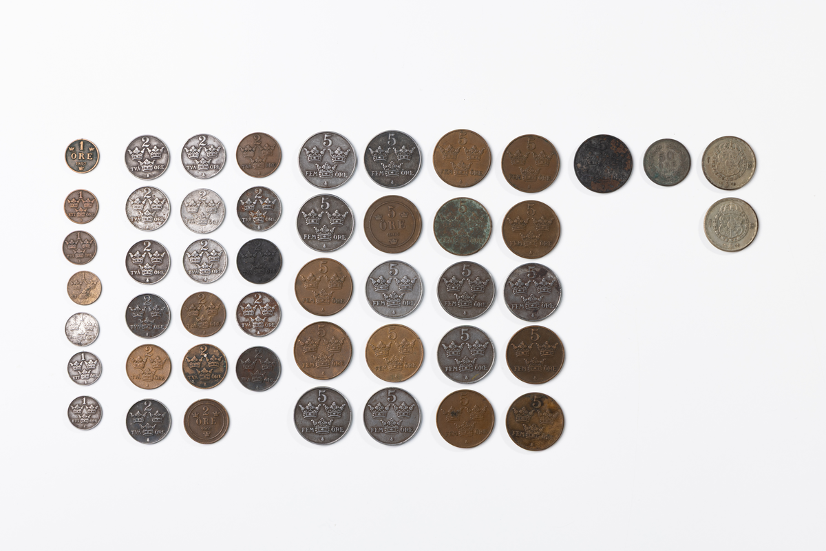Myntapparat för kontant löneutbetalning av metall och plast. Ovanpå knappar med siffror, mitt fram myntrör.

Mynt som ligger i rören:
Enkrona 1 från 1945 och 1948. Totalt 2 enkronor.
Femtioöring, 1 från 1907.
Femöring, koppar, 1 från 1905, 1916, 1925, 1931, 1937, 1938, 6 1950. femöringar, järn, 1 från 1942, 1943, 1946, 1947; 2 från 1948, 1949. 1 från 1950. Totalt 21 femöringar.
Tvåöring, koppar, 1 från 1905, 1910, 1931, 1941, 1950. Tvåöring järn, 1 från 1910, 1942, 1943. 3 från 1945. 1 från 1946. 3 från 1947. 1 från 1948, 1950. Totalt 17 tvåöringar.
Ettöre, koppar, 1 från 1897, 1909, 1926 och en otydlig 1950(?). Ettöre, järn, 1 från 1942, 1944, 1945. Totalt 7 ettöringar.