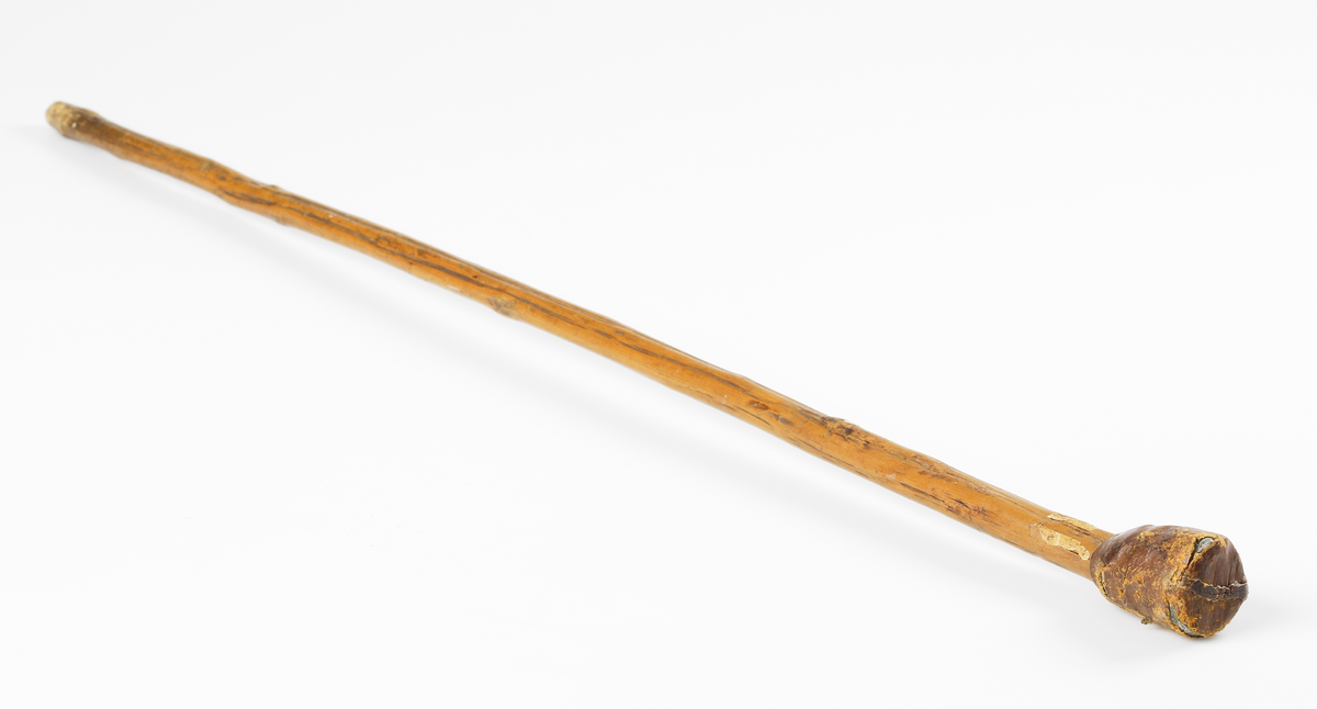 Påk. Käppliknande i trä, med närmast cylindrisk knopp av bly som är omsluten av ett sytt läderhölje.