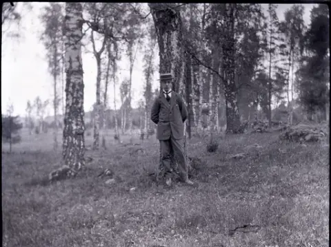 Bengt Stensiö iklädd stråhatt med platt kulle och kostym i en björkhage.