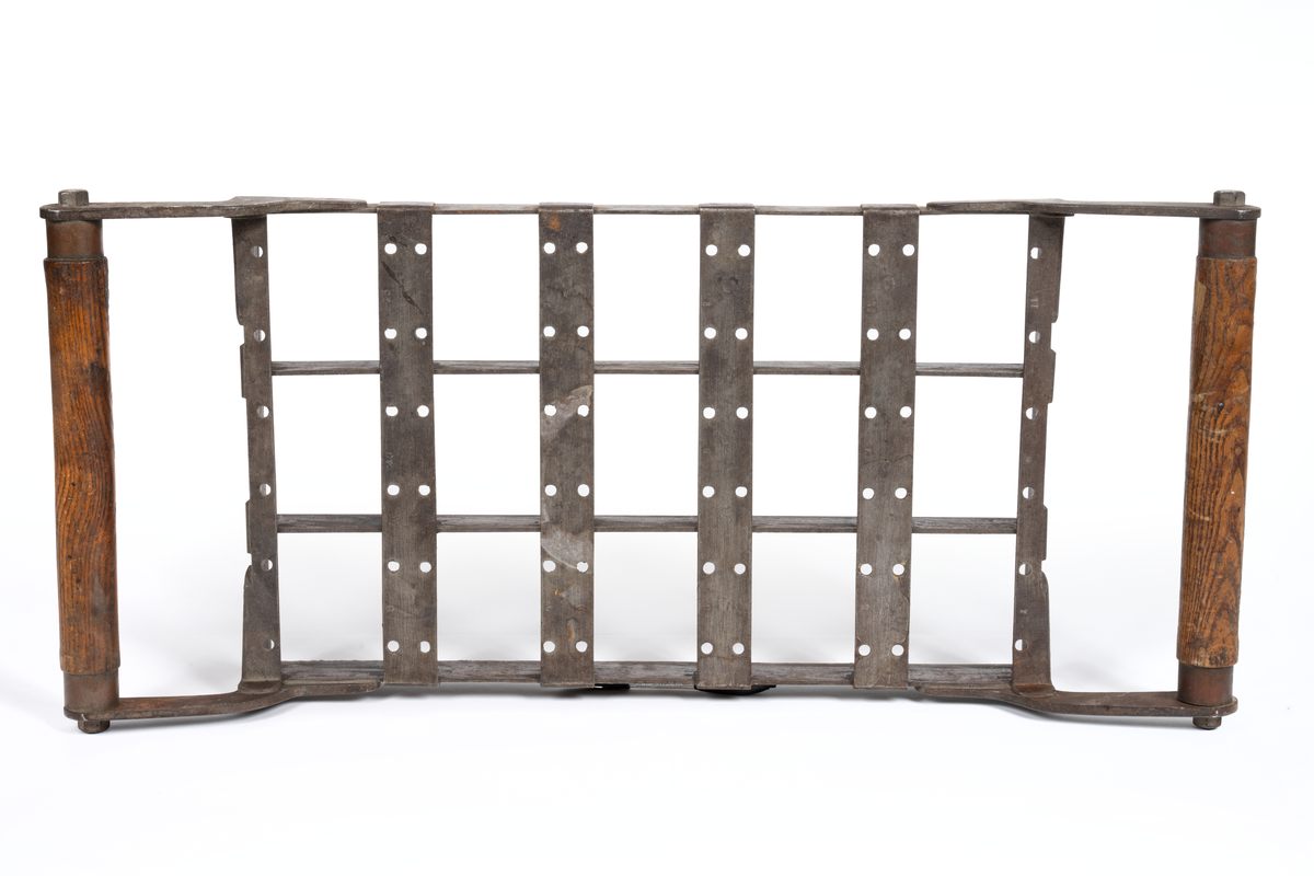 Rektangulär form av järn med två trähandtag längs kortsidorna. Formen är indelad i 15 lika stora rutor. Använd för bakning av skeppsskorpor så kallade knax vid Kronobageriet i Karlskrona.