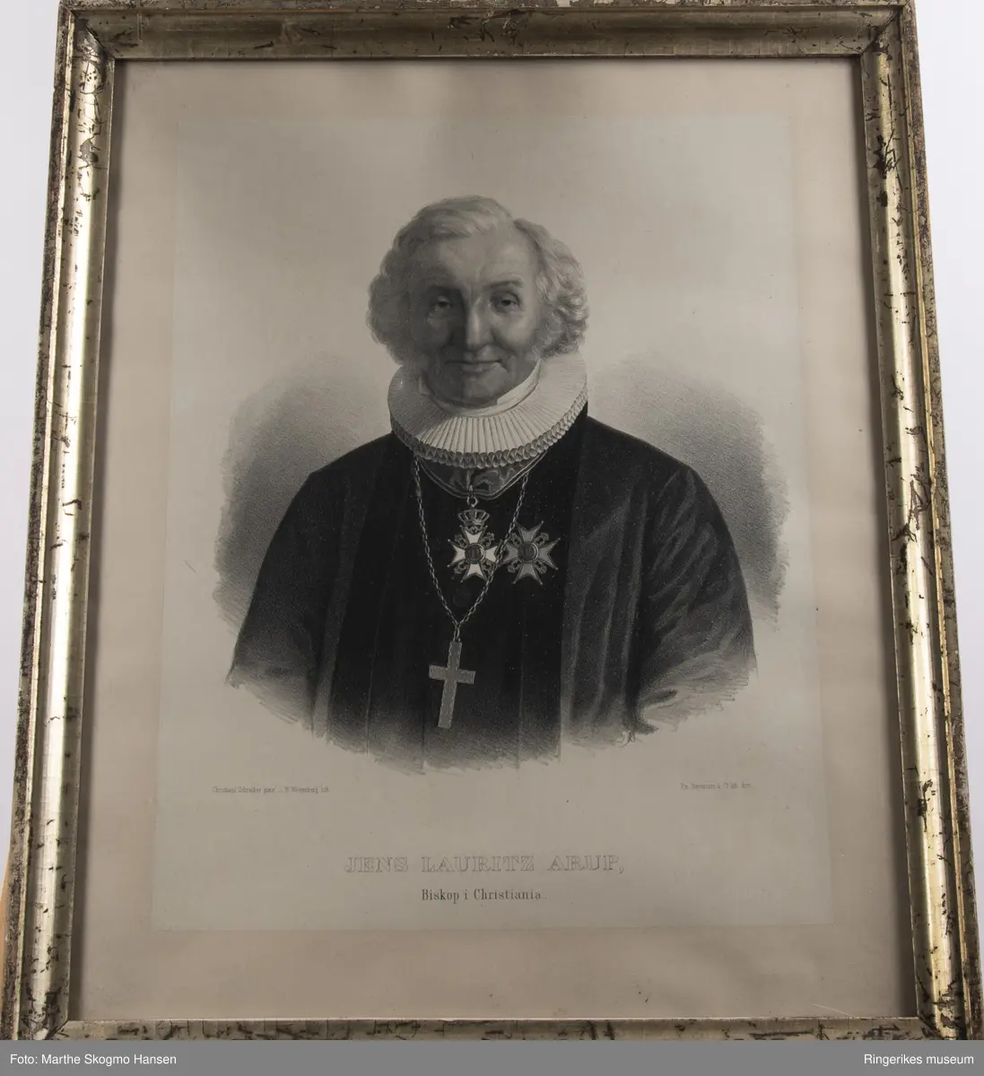 Portrett av en eldre Jens Laurits  Arup, Biskop i Christiania i biskopbekledning med stort kors rundt halsen og medaljer på brystet. Han sitter lett smilende med høytidelig uttrykk i ansiktet og ser rett på tilskueren.