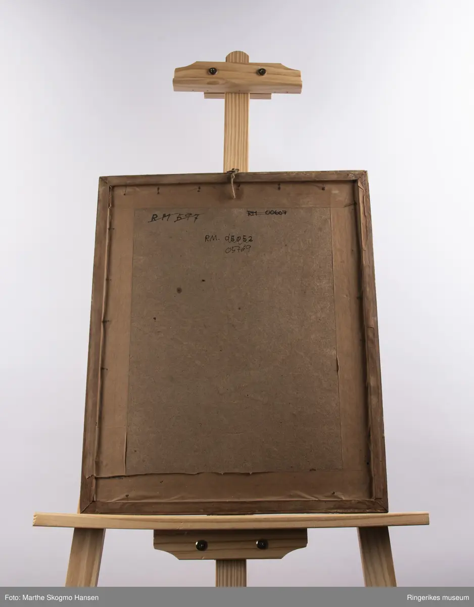 Portrett av en eldre Jens Laurits  Arup, Biskop i Christiania i biskopbekledning med stort kors rundt halsen og medaljer på brystet. Han sitter lett smilende med høytidelig uttrykk i ansiktet og ser rett på tilskueren.