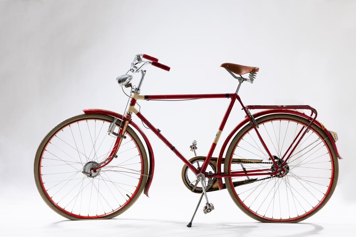 Herrcykel av märket Husqvarna. Ram, stänkskydd och fälgar rödlakerade med vita ränder. Handväxel. Röda plasthandtag, brun sadel. Nyare framlykta med dynamo på sidan. Lås med nyckel och Caltexbricka. 28 tums hjul. Kedjeskydd. Slitna originaldäck av gummi. Mitt fram på ramen ett märke "Husqvarna". På ramen bak märkt: "Sverigeloppsprövad". Ramnr: H 428 296 *.