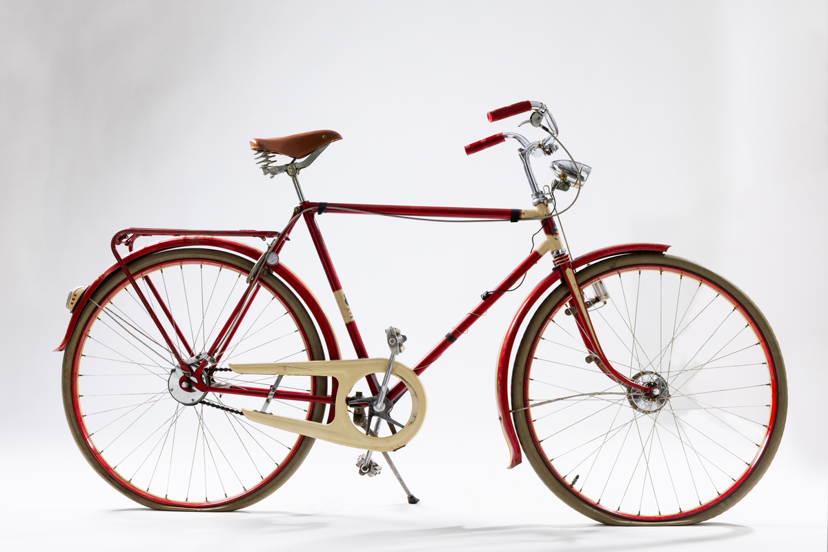 Herrcykel av märket Husqvarna. Ram, stänkskydd och fälgar rödlakerade med vita ränder. Handväxel. Röda plasthandtag, brun sadel. Nyare framlykta med dynamo på sidan. Lås med nyckel och Caltexbricka. 28 tums hjul. Kedjeskydd. Slitna originaldäck av gummi. Mitt fram på ramen ett märke "Husqvarna". På ramen bak märkt: "Sverigeloppsprövad". Ramnr: H 428 296 *.