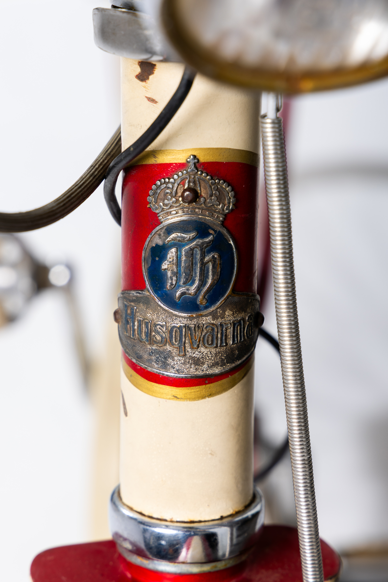 Herrcykel av märket Husqvarna. Ram, stänkskydd och fälgar rödlakerade med vita ränder. Handväxel. Röda plasthandtag, brun sadel. Nyare framlykta med dynamo på sidan. Lås med nyckel och Caltexbricka. 28 tums hjul. Kedjeskydd. Slitna originaldäck av gummi. Mitt fram på ramen ett märke "Husqvarna". På ramen bak märkt: "Sverigeloppsprövad". Ramnr: H 428 296 *.