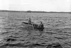Foto av två militärer som ror en primitiv eka (jolle) på Helgasjön (?).
