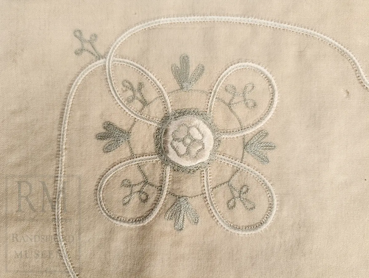 Kvadratisk, tynt ullstoff. Frynser langs alle fire kanter. Brodert motiv i et hjørne, antatt tamburering. 