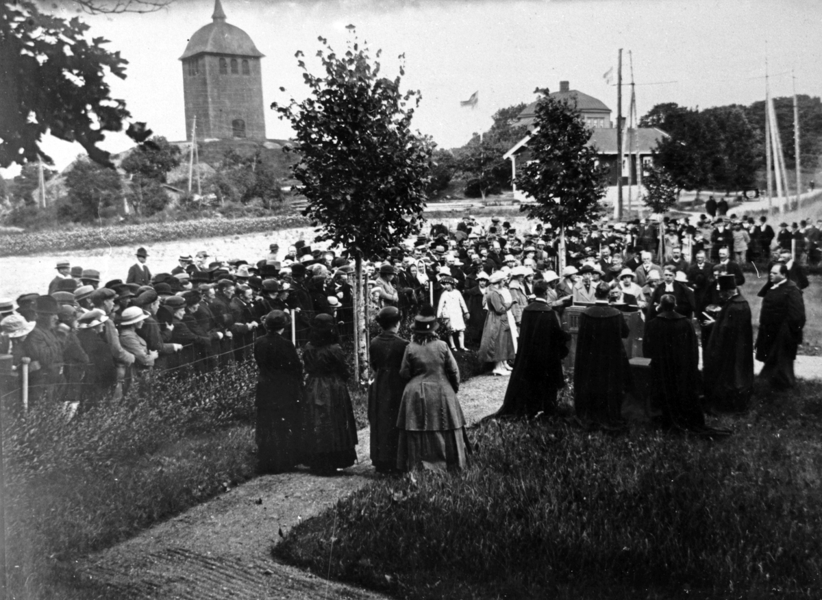 Sorunda kyrka. Vid invigningen av Sorunda nya kyrkogård. En stor grupp människor har samlats vid kyrkogården. I bakgrunden Sorunda klocktorn. 

Religion, högtid.
