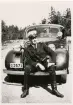 Konstapel Uno Logarn i sommaruniform, sittande på kofångaren till en polisbil, ca 1951.