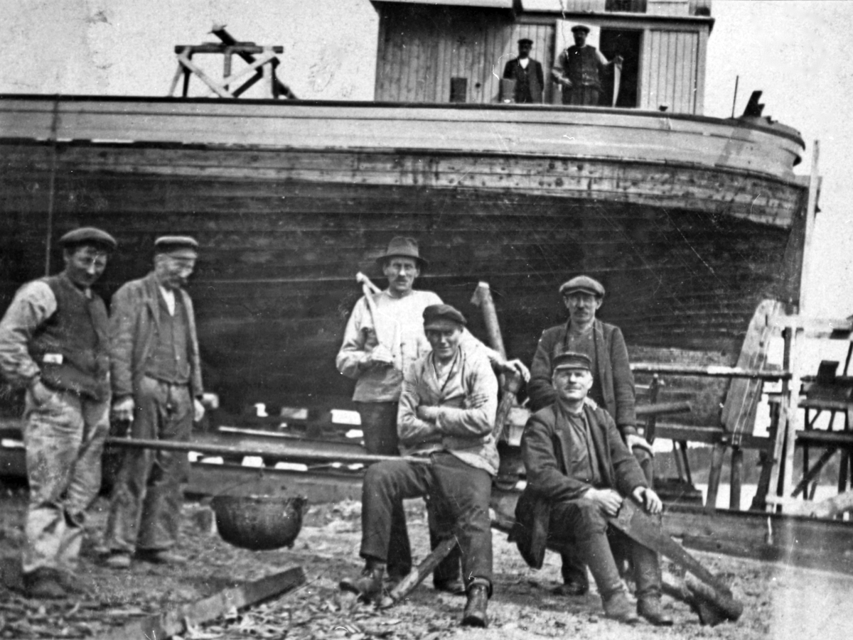 Sex män står framför en båt vid Frejas varv. Männen har verktyg i händerna. 

Yrken, arbete, hantverk, sjöfart, rederi, industri, byggnad.

Personer på bilden:
Från vänster: 1. ?, 2. Rudolf Larsson "Klipp-Lasse", 3. Nils Burman, 4. Lars Schönning, 5. ?, 6. ?