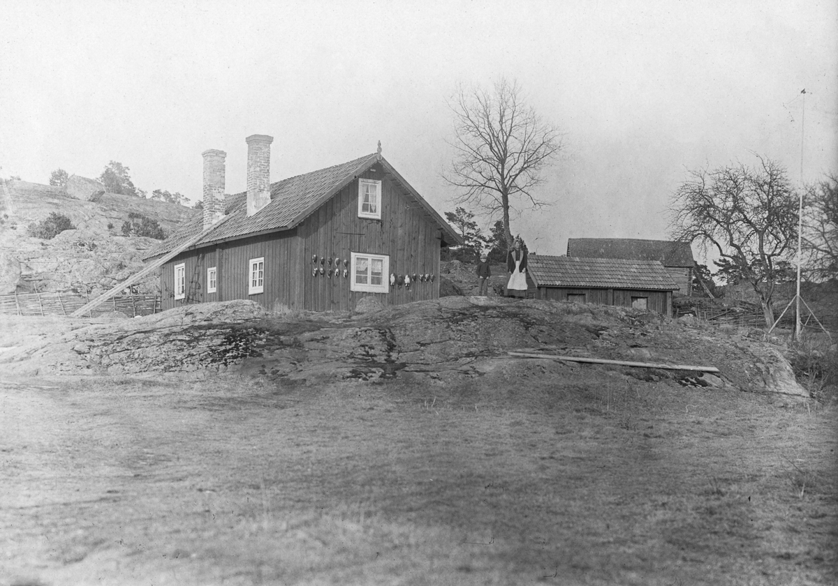 Tattmarstugan med så kallade vettar på gaveln. En pojke och en flicka står på berget vid stugan. 

Skärgård, fågeljakt.