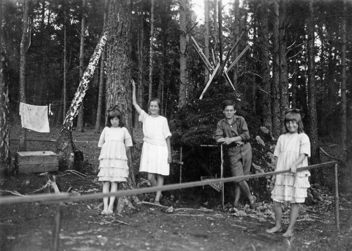 Hos familjen Andersson Gårdsund, Yttre Gården, Bedarön. Fyra barn står framför en skogskoja. 

Skärgård, sommar, lek.

Personer på bilden:
Från vänster: Astrid  Andersson, Margit, Olle, Ingrid Andersson.