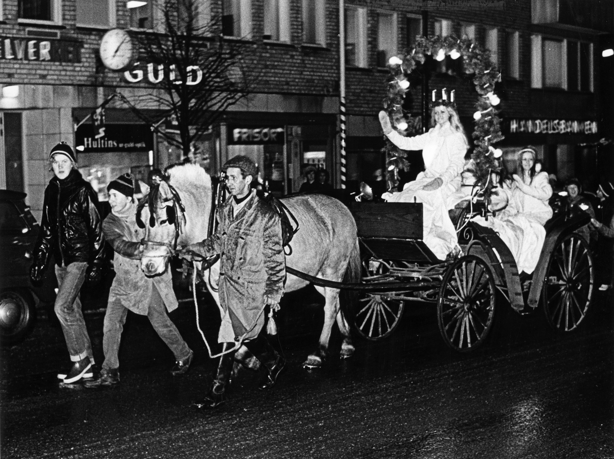 Luciafirande, en luciakortege med häst och vagn åker på Centralgatan i höjd med Hultins guld och Handelsbanken. Fotografiet Luciakortegen ordnades av Nynäshamns ridklubb. 

Tradition, årshögtid, jul, husdjur, fritid, förening, vinter.

Personer på bilden:
Lucia Marianne Olofsson