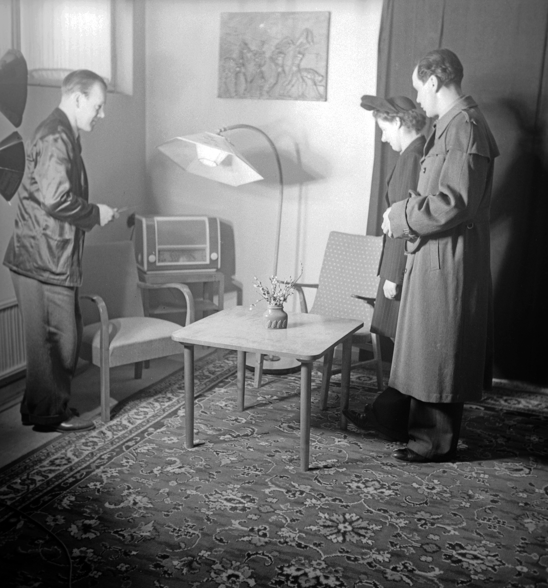 Interiör från Special-Konsum, bosättningsavdelningen. En manlig expedit hjälper ett par att titta på vardagsrumsmöbler.  

Handel, möbler, inredning.