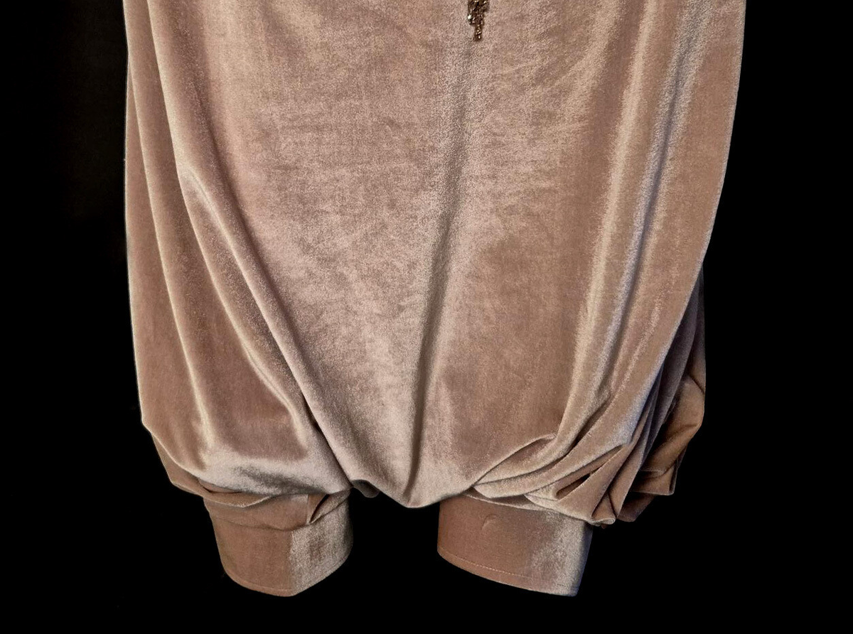 Byxor i harem-modell uppsydda i rosa-beige sammetstyg och champangefärgade applikationer samt stenar. Applikationerna är i form av blommor och löv. Fastklistrade på tyget i en större vertikal form i mitten av byxorna. Ihopsydd med 4 tygpaneler, ej fodrad. Samansatt med raksöm och vid vissa delar overlocksöm. Byxbenen avslutas med muddar som stängs med 2 hakar och hyskor på vardera ben. Muddarna har ett mellanlägg för att ge struktur. Midjan har en kanal för ett vitt snöre som knyts för att dra åt midjan och stänga byxorna. 

